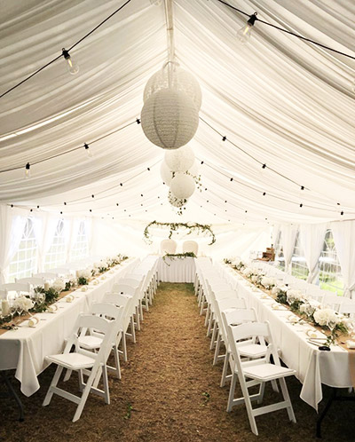 Salle de réception de mariage avec des chaises blanches en bois et des voilages. Mariage campagne bohème champêtre. Décoration fête